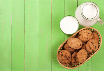 jug and glass of milk with oatmeal cookies on a green wooden background with copy space for your text. Top view