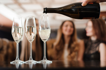 Man fills glasses of champagne for three beautiful young women in restaurant