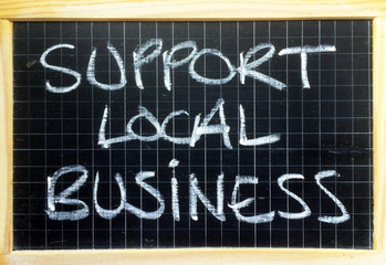 The words Support Local Business written by hand in white chalk on a blackboard as a reminder to buy goods and services in your community