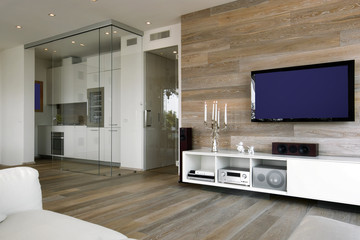 interior view of a modern living room with wooden wainscoting , television and wooden floor overlooking on the kitchen
