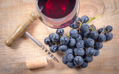 Glass of red wine with a sprig of grapes on a wooden table.