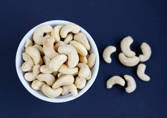 White bowl of cashew nuts. Black background
