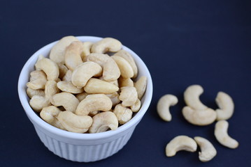 White bowl of cashew nuts. Black background
