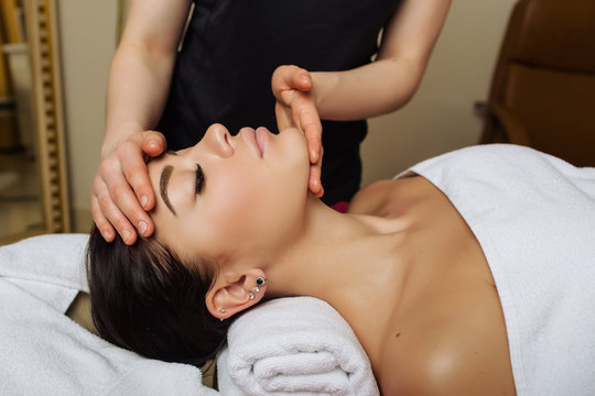 woman with closed eyes receiving face massage lying on a massage table, massage therapist hands working on massaging woman's neck and chin. Rejuvenating facial contour massage