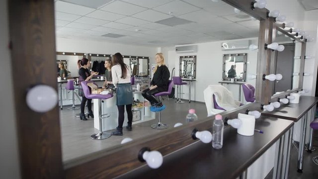 Interior of luxury beauty salon designed in modern style showed from unusual angle. Masters and clients of studio are reflected in a mirror with the lamps during their working together.