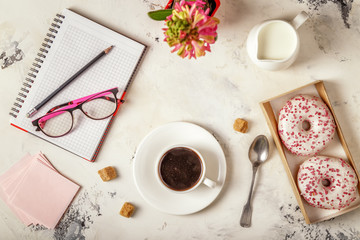Notepad, donuts and coffee on white table.