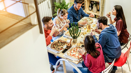 Obraz premium Loft view of happy friends eating pizza and toasting beer at home