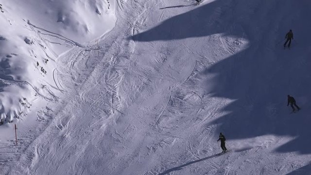 Large group of unrecognizable skiers skiing down the snow covered mountain slope on sunny winter day in ski resort