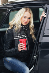 Fototapeta na wymiar Young woman with a red cup sitting in the car