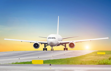 Naklejka premium Duży samolot na kołowaniu o zachodzie słońca na lotnisku, niebo jest słońcem i torem sterowym