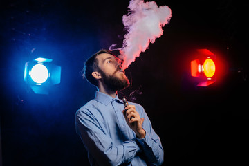 Young guy with a beard vaping and releases a cloud of vapor. hipster vaper smoke vaporizer.
