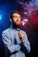 Young guy with a beard vaping and releases a cloud of vapor. hipster vaper smoke vaporizer.