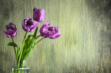 Spring tulips in a glass jar on a wooden background