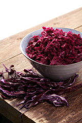 Shredded red cabbage in clay bowl on wooden background. Vegetari