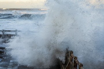 Waves from high Spring Tide crashing over the barrires of the old, disused swimming pool at...