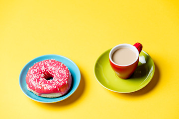 tasty glazed donut and cup of coffee on plates on the wonderful yellow background