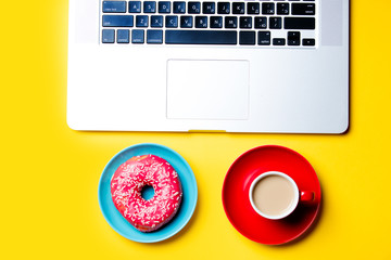 laptop, tasty glazed donut and cup of coffee on plates on the wonderful yellow background