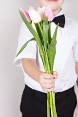 Bouquet of spring flowers in children's hands. Tulips, irises - early spring flowers is holding a child. Greetings from the boy in smart clothes. Mother's Day, Women's Day, gift, a bouquet of flowers.