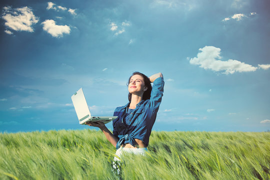 beautiful young woman with laptop standing in the middle of the wonderful green field