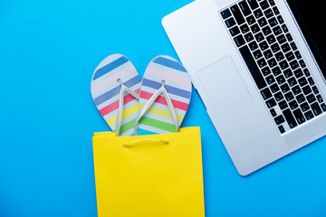 colorful sandals in shopping bag and cool laptop on the wonderful blue background