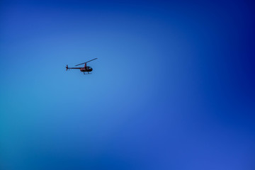 Military helicopter flying in the sky over a city and crowded event, taking photos, filming from above on clear blue sky background. An Isolated helicopter. Team of rescuers searching for lost people