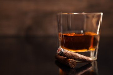 Smoking cigar next to the glass of whiskey