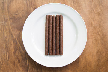 wafer rolls with chocolate in white plate on wooden table.