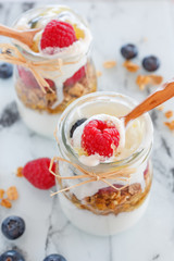 breakfast with yogurt and cereal flakes and raspberries with blueberries. a mixture of yogurt, cereal, berries in portion glass jar and wooden spoons. Rustic food background