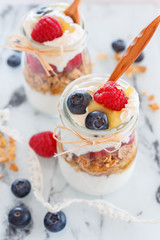breakfast with yogurt and cereal flakes and raspberries with blueberries. a mixture of yogurt, cereal, berries in portion glass jar and wooden spoons. Rustic food background