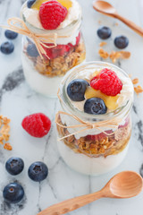 breakfast with yogurt and cereal flakes and raspberries with blueberries. a mixture of yogurt, cereal, berries in portion glass jar and wooden spoons. Rustic food background