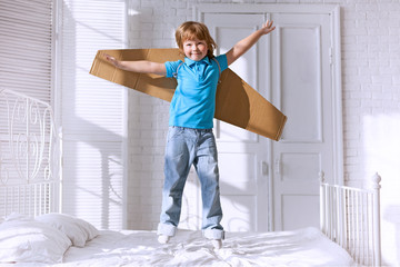 Fototapeta na wymiar child with cardboard wings jumping on bed in the bedroom