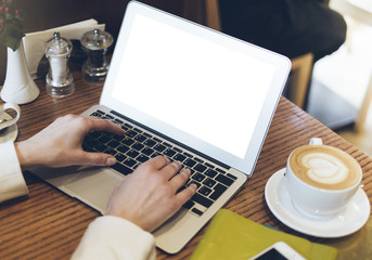 Woman writing text on open laptop on wood table with empty blank screen monitor at home, person drink cup of coffee on background atmosphere cafe, female hands working on computer, mockup templates
