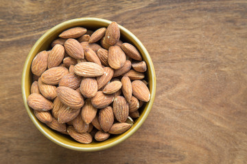 Almonds in bowl on wooden background, top view.