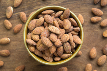 Almonds in bowl on wooden background, top view.