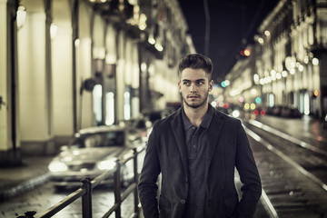 Attractive young man portrait at night with city lights behind him in Turin, Italy