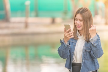Fototapeta premium Success and Surprised young Asian woman using smart phone outdoors.Girl happy She was glad to get good news