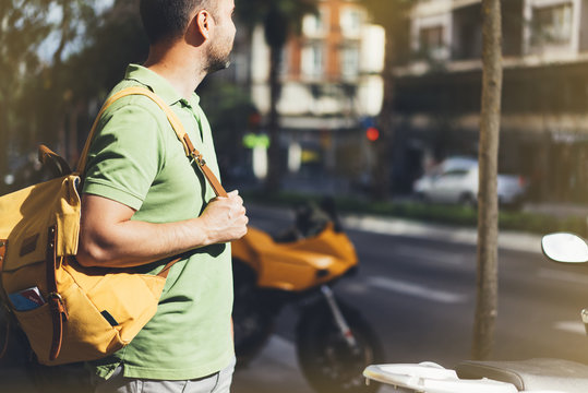 Hipster man holding in hands backpack and map. Side view tourist traveler planning route on background sun and orange motorcycle. Person visiting the sights city on backdrop summer street