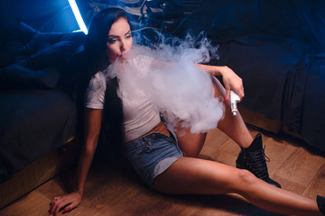 Sexy brunette vaping vaponizer and clouding, woman with sexy body at blue lights background