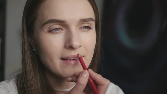 Beautiful attractive girl makes herself makeup, red pencil encircles the contour of the lips, slow motion