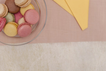 Yellow and pink macaroons french sweets on yellow and pink napkins with colorful macarons (macaroons) in a glass bowl in the background from above.