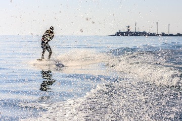 Wakeboarder glides on sea surface hauled by motorboat with splashes scattering around. Outdoor extreme sport and leisure activities at summer resort