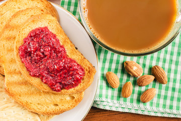 Breakfast time, cup of coffee with milk and toasts with raspberry jam on napkin, top view.
