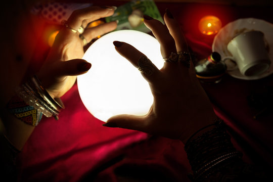 Hands of fortune teller woman above illuminated crystal ball