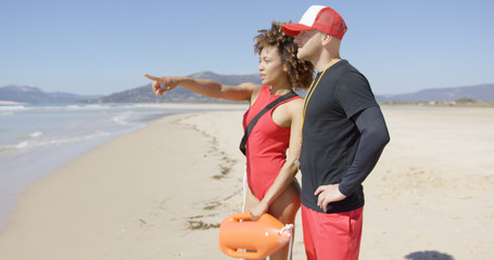 Female lifeguard pointing with finger into distance standing on beach with male. Tarifa beach....