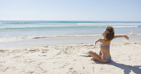Female wearing two-piece swimsuit sitting with arms outstretched to sides on beach. Tarifa beach. Provincia Cadiz. Spain. 