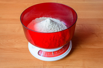 Analog red kitchen scales on the wooden table. Preparation for baking. Kitchen tools. Bowl with...