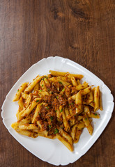 pasta penne with stew meat sauce in a plate on wooden table. with copy space. top view