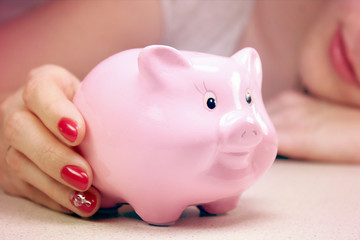 Young woman smiling and holding a piggy bank on a table hand