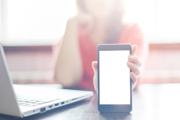 Portrait of female freelancer showing pictures on mobile phone with blank copy space screen for your text or advertising content while sitting at the wooden table near her laptop. Selective focus