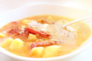 Appetizing pea soup with potatoes and meat close-up